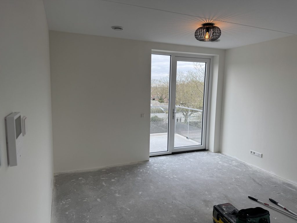 Lichte kamer met gladde witte wanden, een balkondeur en een plafondlamp, kort na de afwerking